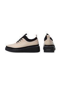 Beige- und schwarze Schnürschuhe mit einer strukturierten Gummisohle, schlankem Design, runder Zehenform und einem kleinen Absatz, versehen mit einem Logo auf der Rückseite.