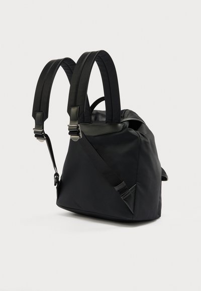 Μαύρο μαλακό ύφασμα σακίδιο με επενδυμένους ρυθμιζόμενους ιμάντες ώμου και μεταλλικά κουμπώματα σε απλό φωτεινό φόντο.