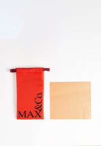 Monedero rojo con "MAX & Co." en texto negro, hecho de una tela brillante. Tela cuadrada beige al lado, que presenta un patrón grabado de "MAX & Co.".