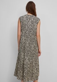 Vestido negro midi con patrón floral blanco, mangas cortas, detalle de ojal en la espalda y sección de falda con volantes. Hecho de tela ligera.