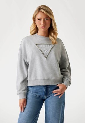 Grijze sweatshirt met een opvallend driehoekig logo in zilver met kristalaccenten. Losse pasvorm met geribde manchetten en onderrand. Gepaard met blauwe jeans.