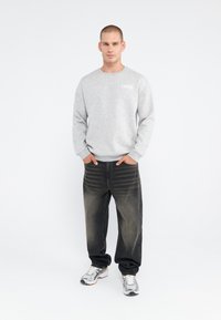 Grå sweatshirt med logo, afslappet pasform, ribbede manchetter, parret med mørke denim jeans, let slidte, og grå sneakers.