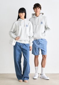 Light gray hoodies with front pockets and drawstrings, paired with blue denim jeans and shorts. Notable white sneakers worn by both.