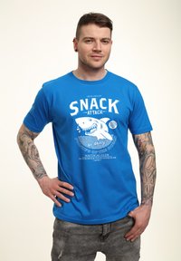 Modrá bavlněná tričko s grafickým designem žraloka, textem "SNACK ATTACK" a námořními prvky. Krátké rukávy a kulatý výstřih.