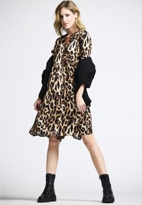 Kleid mit Leopardenmuster, ausgestelltem Saum, kurzen Ärmeln und lockerer Passform. Kombiniert mit schwarzen Combat-Stiefeln und einer strukturierten schwarzen Strickjacke.