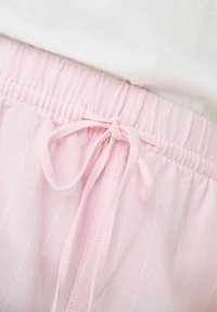 Pantalons avec une taille élastique rose et des rayures verticales blanches, dotés d'un lien de serrage. Tissu doux avec une texture lisse.