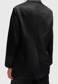 Černý blazer s hladkým povrchem, jedním zadním rozventem a detaily na manžetách se šesti knoflíky. Vyznačuje se klasickým střihem a strukturovaným tvarem.
