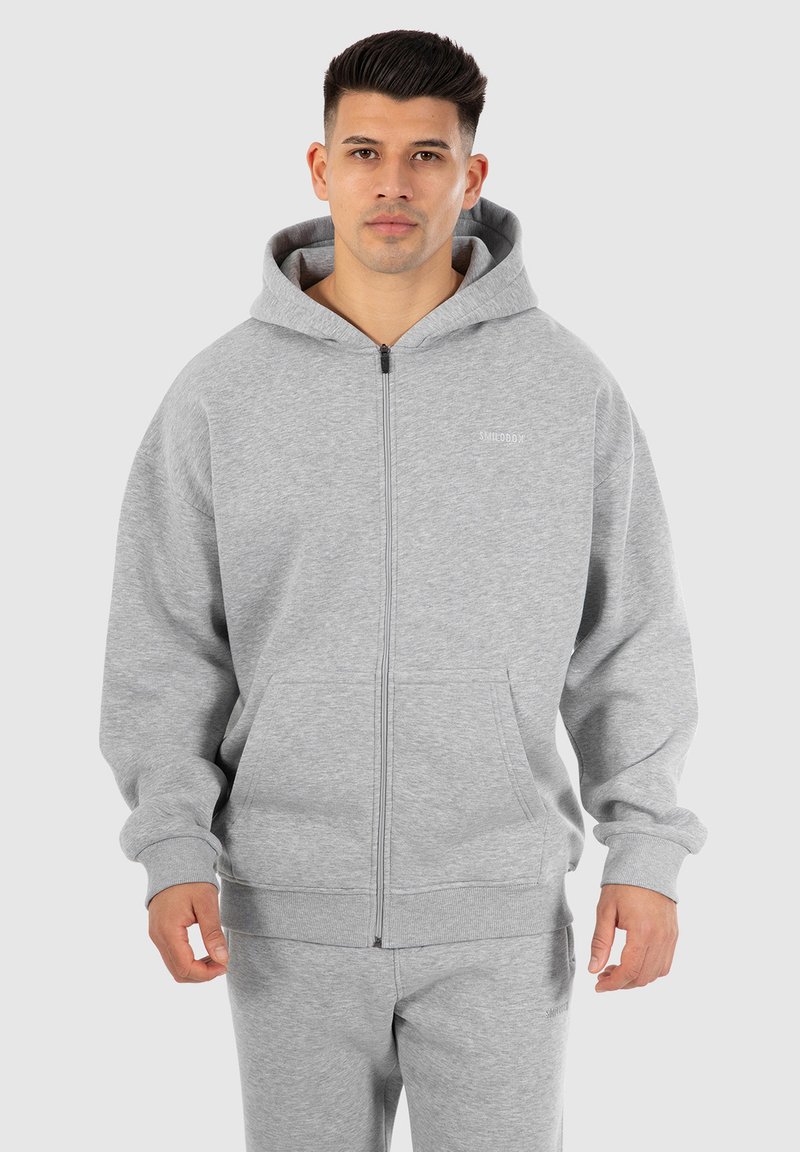 Ljusgrå zip-up hoodie gjord av mjukt, texturerat tyg. Har en dragsko i huvan och kängurufickor. Subtil logotyp på bröstet.