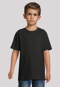 Black cotton t-shirt with short sleeves, crew neck design, and a smooth texture. Model stands with arms relaxed at sides, wearing denim jeans.