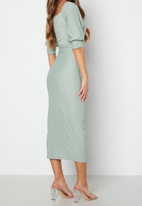 Robe midi côtelée vert menthe avec manches bouffantes et décolleté carré, associée à des sandales à talons transparents ; texture lisse et près du corps.