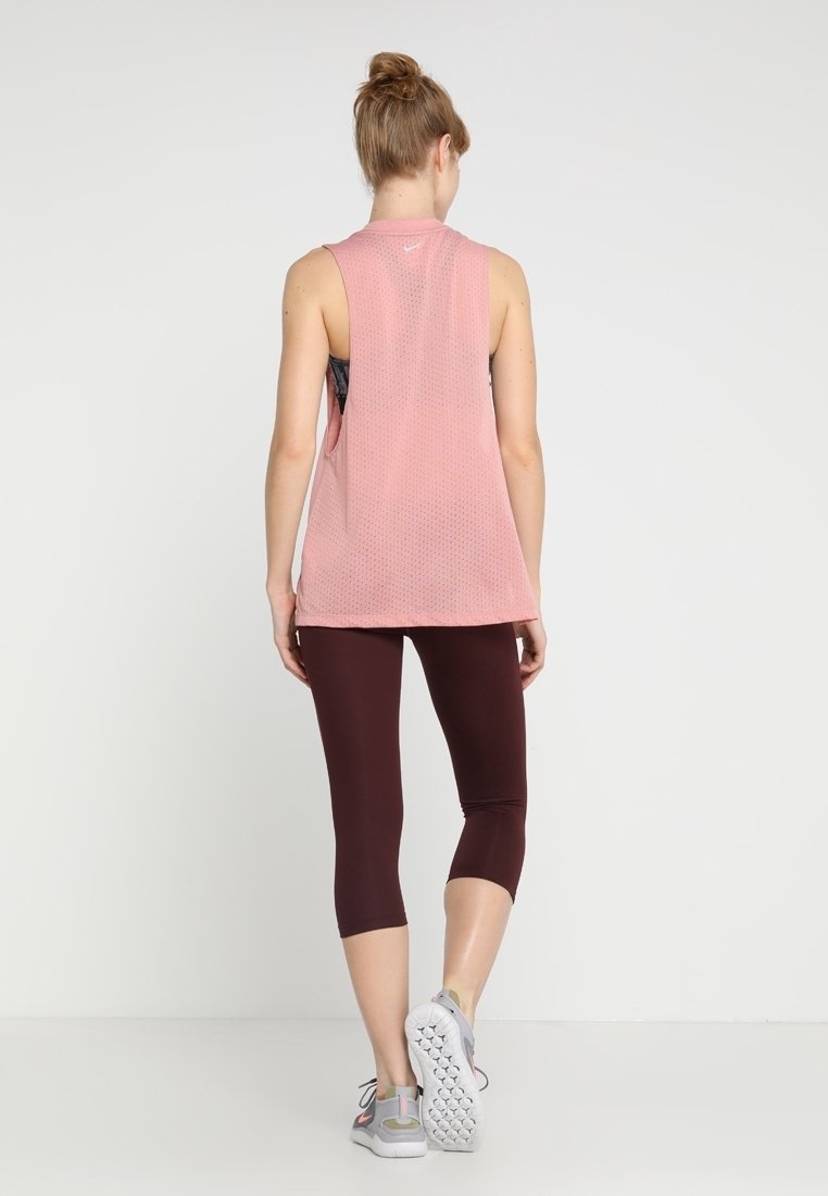 Roze lichtgewicht mesh tanktop met een uitsnede op de rug, gecombineerd met bordeauxkleurige capri legging. Heeft grijze sportschoenen.