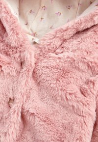 Giacca di pelliccia finta rosa con una texture morbida, caratterizzata da una chiusura a bottone e un rivestimento interno con motivo floreale in colori tenui.