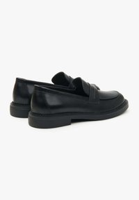 Zwarte leren loafers met een lage profiel, ronde neus en gestikt detail langs de zool; voorzien van een brede band over de wreef.