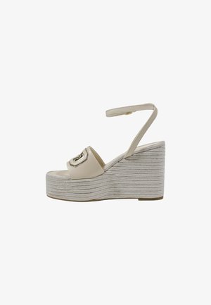Sandalias de cuña beige con una parte superior de cuero suave, correa ajustable en el tobillo y una plataforma estilo espadrille trenzada. Detalle de herrajes en tono plateado en la parte delantera.
