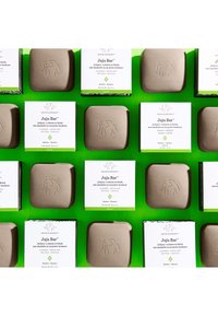 Brown Juju Bar soap with an elephant imprint and white packaging displaying product details, arranged on a bright green background.