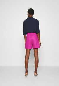 Shorts i klart rosa linne med avslappnad passform, tillsammans med en mörkblå skjorta med krage och silverfärgade klacksandaler. Enkelt design med minimalistiska detaljer.