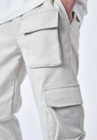 Pantaloni cargo beige chiaro con molteplici tasche laterali, realizzati in tessuto intrecciato. Presentano una vestibilità dritta e una texture liscia.