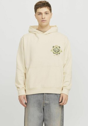 Beige Kapuzenpullover mit einer vorderen Kängurutasche und einem dekorativen grünen und gelben Emblem auf der linken Brust. Weicher Stoff.