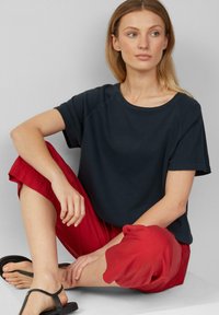 Marineblauwe t-shirt met korte mouwen en een ronde halslijn, gecombineerd met losse rode cropped broek en zwarte sandalen. Simpele, casual outfit.