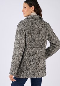 Manteau texturé noir et blanc avec un col structuré, des manches longues et des poches latérales. Présente un motif tissé distinctif et une coupe ajustée.