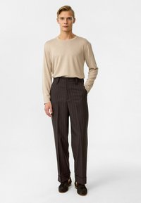 Beige ribben shirt met lange mouwen en donkergrijze gestreepte high-waisted broek. De broek heeft een knoopsluiting en opgerolde mouwen. Bruine schoenen.