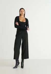 T-shirt noir à manches longues avec un design texturé, associé à un pantalon large noir. Complet avec des bottines à talons hauts noires.