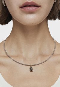 Collar de plata con un diseño suave y minimalista. Presenta un pequeño charm en forma de oso de peluche en tono dorado como detalle notable.