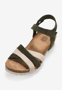 Sandalía de color verde oscuro y beige claro con dos correas anchas, plantilla de corcho y suela texturizada. Talón cerrado con correa de tobillo ajustable.