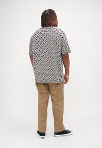 Kortermet svart og hvit mønstrete skjorte, tan cargo bukser, og svarte joggesko. Skjorten har et geometrisk trykk og løs passform.