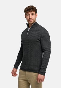 Mörkgrå kabelstickad tröja med hög krage och halvdragkedja, med ribbade muddar och ett texturerat mönster.