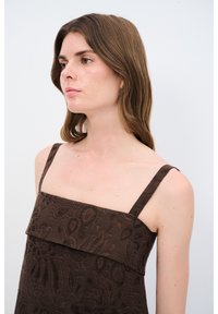 Brun kjole med blomsterprint, firkantet halsudskæring og tynde stropper. Stof med struktureret design. Model vist fra siden.