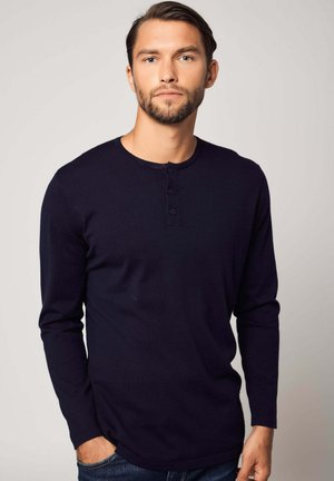 Navyblaues Langarm-Henley-Shirt aus weichem Stoff, mit rundem Halsausschnitt, einer Drei-Knopf-Leiste und einem leichten Saum am unteren Ende.