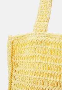 Geel gehaakte tote bag met een dikke geweven strap, gedetailleerd tegen een witte achtergrond.