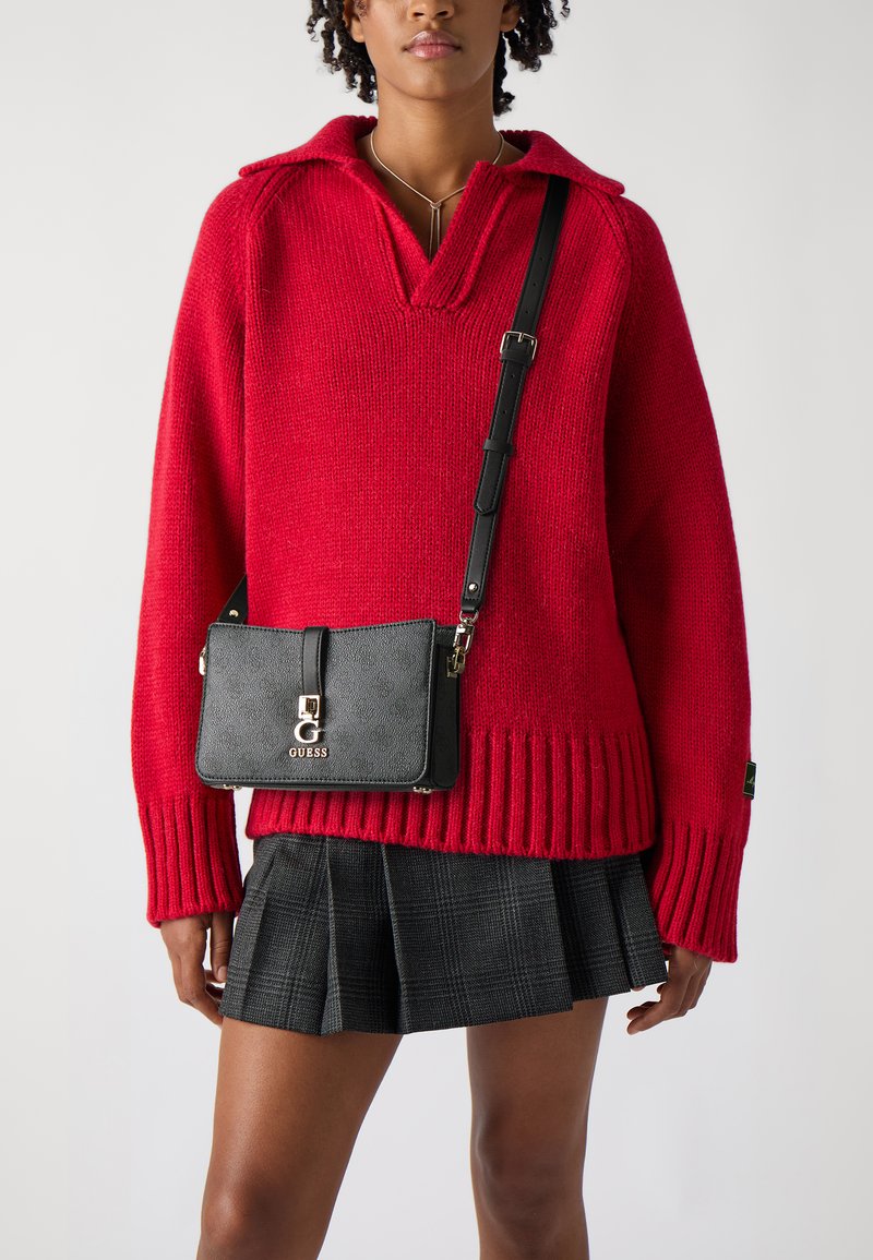 Übergroßer roter Strickpullover mit Kragen, kombiniert mit einer schwarzen Umhängetasche mit Logo und strukturiertem Oberflächen über einem karierten Rock.