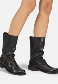 Bottines en cuir noir avec un design plié et un petit talon empilé. La tige présente une finition lisse et un bord supérieur légèrement effiloché.