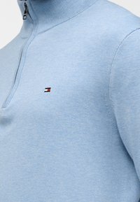 Φουτερ πλεκτό ανοιχτού μπλε χρώματος με φερμουάρ στο 1/4 και μικρό ορθογώνιο κόκκινο, λευκό και ναυτικό λογότυπο στο αριστερό στήθος.