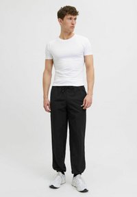 T-shirt blanc à manches courtes associé à un pantalon noir à cordon de serrage, avec une texture légère et un logo discret, complété par des baskets blanches.