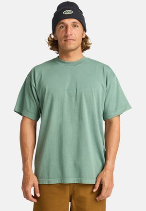 Mint green short-sleeve t-shirt with a round neckline and subtle logo embroidery at the center. Soft fabric, relaxed fit, paired with tan pants.