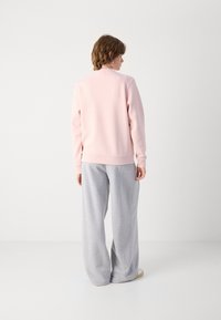 Ljust rosa sweatshirt med rund halsringning och ribbad nederkant, kombinerad med lösa grå sweatpants. Tyget verkar mjukt och bekvämt.