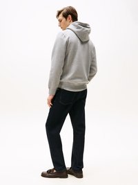 Hoodie cinza de algodão com capuz, combinado com jeans escuros de denim. Sapatos mocassins de sola de borracha completam o visual casual. Fundo liso.