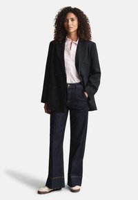 Blazer negru cu nasturi dubli, cămașă cu dungi roz deschis, pantaloni evazați din denim închis cu cusături în contrast, adidași crem și maro.