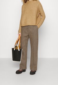 Maglione marrone a maglia, pantaloni a gamba larga a scacchi marroni e neri, borsa a tracolla bianca e nera con manici marroni, scarpe chunky nere.