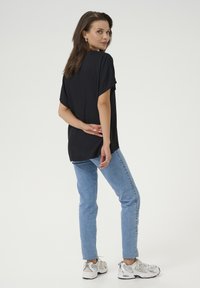 Haut noir à manches courtes avec une coupe décontractée, associé à un jean bleu clair. Le mannequin porte des baskets blanches, affichant un look décontracté et contemporain.