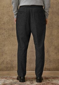 Schwarz gepunktete Hose mit legerem Schnitt, ausgestattet mit einem Bund und zwei Gesäßtaschen. Glatter Stoff mit einer subtilen Textur.