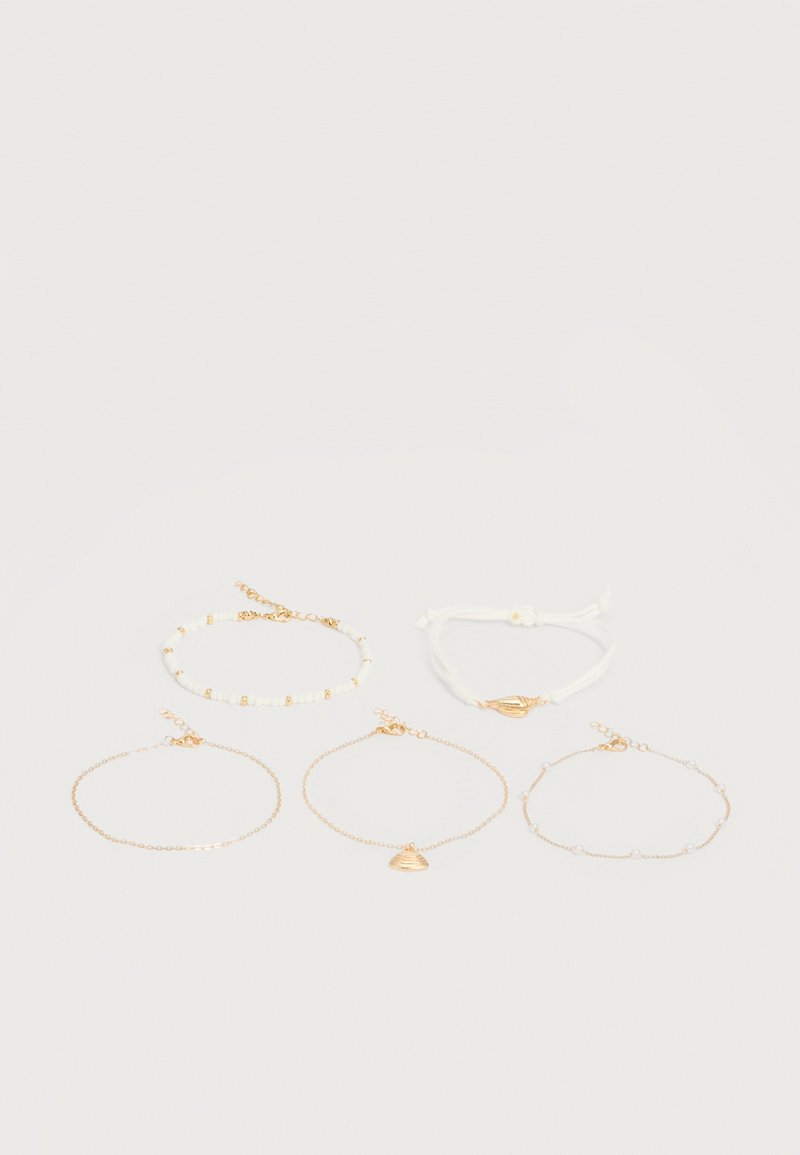 Πέντε λεπτά βραχιόλια σε χρυσό και λευκό χρώμα με μικρές χάντρες και γοργονίσιο φυλαχτό, τοποθετημένα σε φωτεινή επιφάνεια σε δύο σειρές.