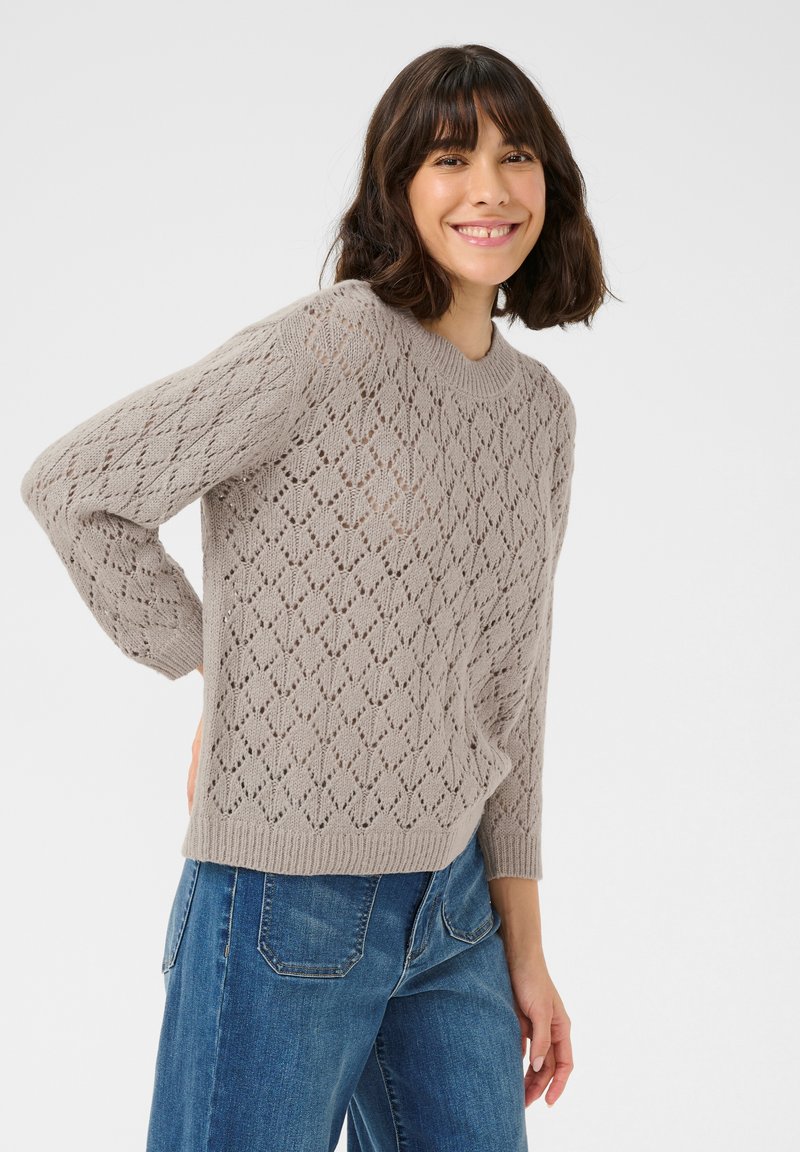 Maglione grigio chiaro lavorato a maglia con motivo a diamante in pizzo, colletto a girocollo a coste e maniche di lunghezza media, abbinato a jeans in denim blu.