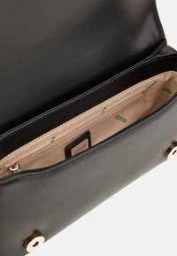 Borsa a tracolla nera in ecopelle con interni beige, dotata di una tasca con zip e un'etichetta con logo. Accenti in metallo color oro.