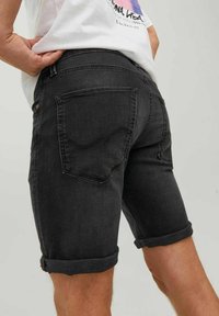 Pantalones cortos de mezclilla negra con puños enrollados, que cuentan con dos bolsillos traseros y una textura sutilmente descolorida. Combinados con una camiseta blanca.