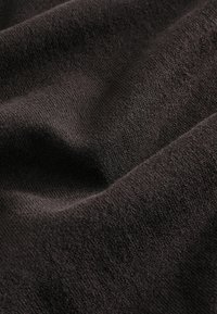 Dunkelbrauner Strickstoff mit einer weichen Textur, der eine glatte Oberfläche und subtile Variationen in der Fadendichte aufweist.