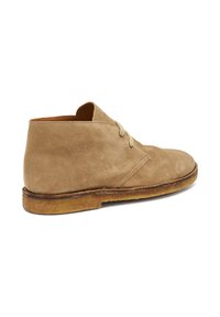 Stivale chukka in suede marrone chiaro con due lacci, suola leggermente usurata, mostrato di lato su uno sfondo bianco.